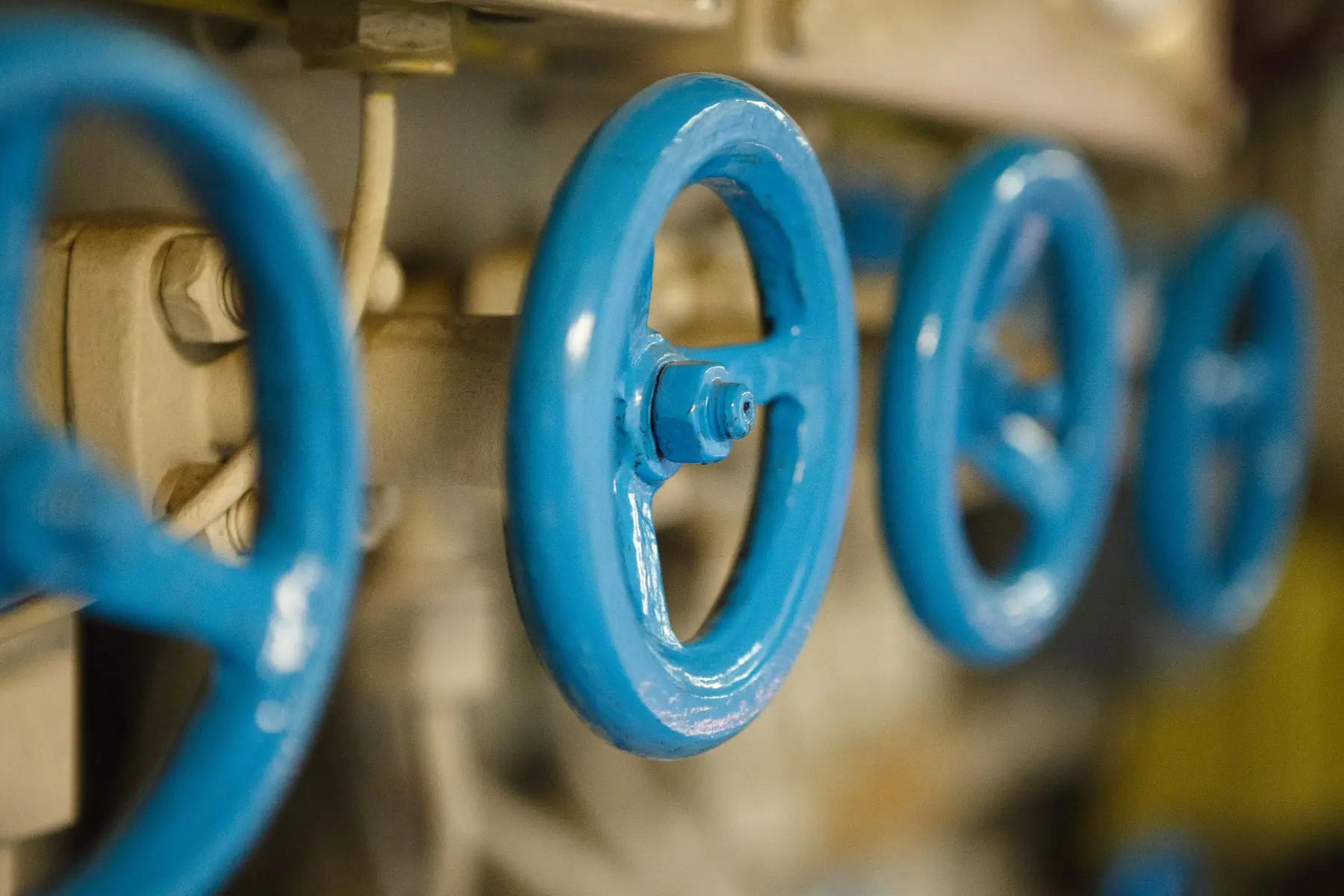 A row of blue valve handwheels on piping, one in sharp focus